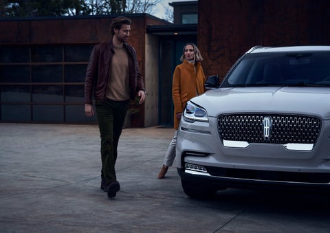 A man and a woman approaching a 2024 Lincoln Aviator® SUV, which illuminates certain lights when they are close | Vision Lincoln in Wahpeton ND