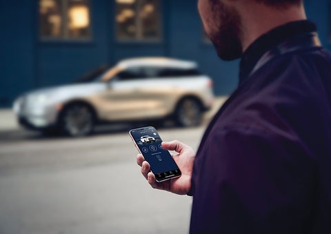 A person is shown interacting with a smartphone to connect to a Lincoln vehicle across the street. | Vision Lincoln in Wahpeton ND